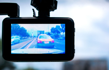 Car dashcam display showing a road scene with vehicles and trees under a cloudy sky.