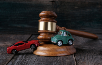 Two toy cars, one red and one green, are positioned on a wooden gavel and sound block, symbolizing legal issues related to traffic or accidents.