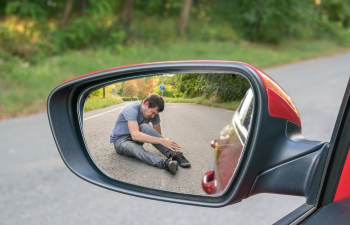 Person sitting on the road, adjusting shoe, reflected in a car's side mirror.