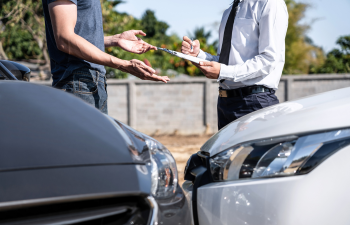 Two men stand between two cars discussing a document on a clipboard, likely addressing a car collision.