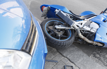 A blue motorcycle is lying on its side next to a blue car, showing signs of a collision on a paved surface.