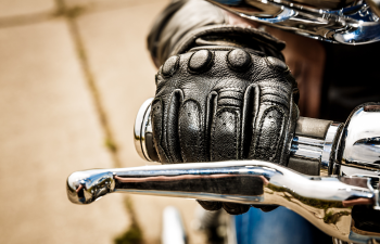 A gloved hand grips the throttle of a motorcycle, with chrome handlebars and a visible clutch lever.