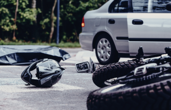 Motorcycle accident scene with a fallen bike, a helmet on the road, and a car parked nearby.