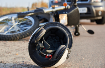 A motorcycle and helmet lie on the road near a car after an accident.