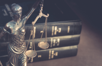 Bronze Lady Justice statue holds scales in front of stacked law books.