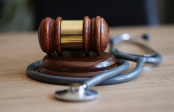 A judges' gavel rests on a wooden block, surrounded by a stethoscope on a table.