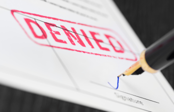 A pen signs a document stamped with "DENIED" in red ink.