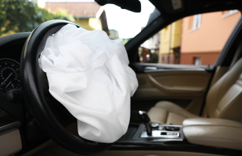 Deployed airbag in a car's driver seat, showing interior with steering wheel and dashboard.