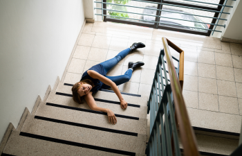 Person lying on a staircase landing, with one arm extended and eyes closed, wearing jeans and a black shirt.