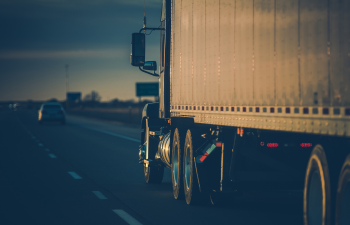 A large semi-truck drives on a highway at dusk, with other vehicles visible in the distance.